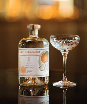 深色表面上的 St George Atlas Orange Gin 酒瓶和 coupe 杯，帶有溫暖燈光。 — Motorola Razr Ultra 2026 壁紙