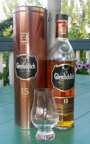 Glenfiddich 15年威士忌瓶和杯子放在戶外的綠色桌子上。 — Galaxy Tab Active 壁紙