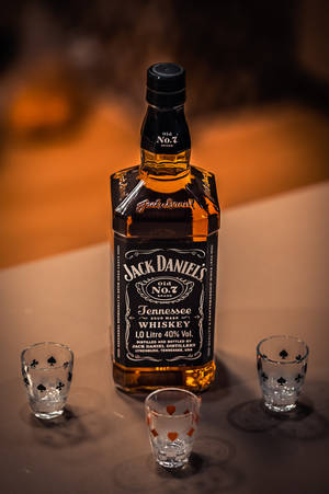 一瓶Jack Daniel's威士忌，配三個烈酒杯，放在桌子上。 — 小米平板 9 Pro Max 壁紙