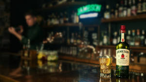 Jameson威士忌酒瓶和玻璃杯在吧檯上，背景有調酒師 — 酒吧 壁紙