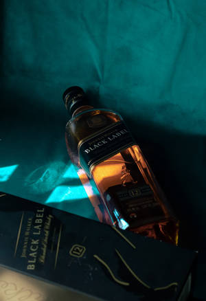 Johnnie Walker Black Label威士忌酒瓶和盒子放在青綠色布料上，帶有戲劇性的燈光。 — IQOO Pad5 壁紙
