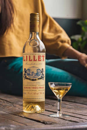 一瓶Lillet法國開胃酒和一個酒杯放在木桌上，後面坐著一個人。 — 葡萄酒 壁紙