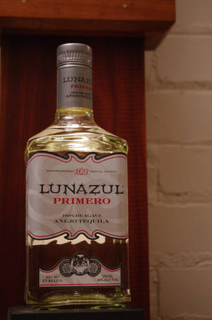 一瓶Lunazul Primero Añejo龍舌蘭酒在一個磚和木背景的架子上。 — 品牌 壁紙