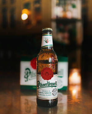 一瓶Pilsner Urquell啤酒在木製吧檯上，燭光氛圍。 — 啤酒 壁紙