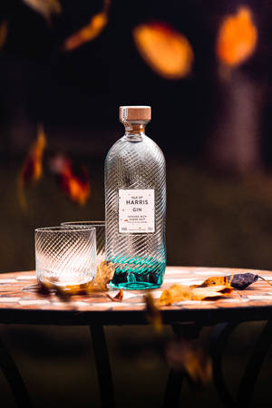 在溫暖的傍晚光線下，馬賽克桌上放著一瓶琴酒和玻璃杯，伴隨著秋葉。 — 小米平板 7S Pro 12.5 壁紙