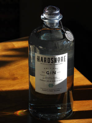 木桌上的一瓶Hardshore琴酒，陽光營造出彩虹稜鏡效果。 — 3:4 壁紙