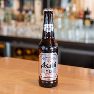 Asahi Super Dry 啤酒瓶放在木吧檯上，背景模糊的酒吧。 — 啤酒 壁紙