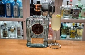 Brooklyn Gin 酒瓶和雞尾酒放在木製吧檯上，背景有酒瓶。 — 精細 壁紙