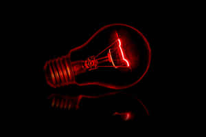 一盞發光的紅色燈泡在暗色表面上的倒影。 — 省電 壁紙