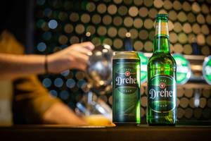 吧檯上的兩個 Drehe Gold 啤酒容器，背後有調酒師在倒飲料。 — 啤酒 壁紙
