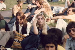 穿著1970年代嬉皮風格的年輕人坐在戶外活動的草地上。 — Woodstock 壁紙