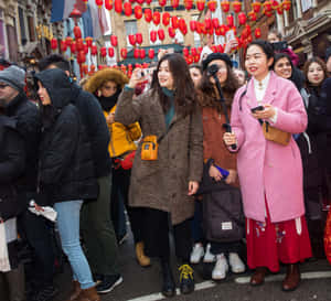 穿著冬季外套的人們在繁忙街道的紅燈籠下拍照。 — 春節 壁紙