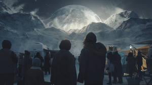 穿著冬季裝備的人們在黃昏時仰望雪山上空的一顆巨大發光行星。 — 月落 壁紙