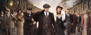 一群1920年代的幫派分子穿著大衣和帽子走在磚街上。 — Peaky Blinders 壁紙