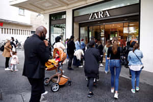 購物者在Zara商店外面，推著嬰兒車在人行道上排隊。 — Zara 壁紙