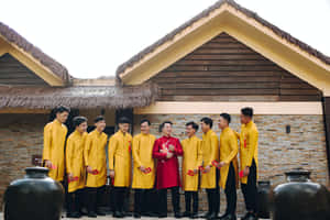 身穿黃色和紅色傳統服飾的男子在戶外茅草屋頂建築附近微笑。 — 婚紗 壁紙