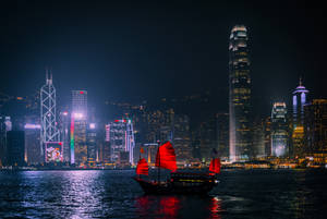 水上紅色帆船，背後是燈火通明的城市天際線 — 香港 壁紙