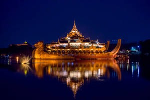 夜晚漂浮在水面上的燈光寺廟船，帶有金色倒影。 — 日式龍 壁紙