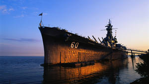 一艘大型戰艦在日落時停泊，溫暖的光線反射在水面上。
