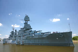 灰色戰艦，甲板上有人的，漂浮在棕色水上，藍天下 — 海軍藍 壁紙