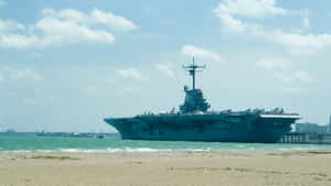 一艘大型灰色航空母艦停泊在沙灘附近，海面平靜，天空多雲。 — 德州 壁紙