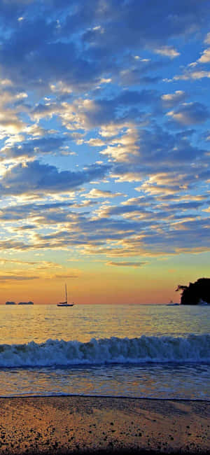 平靜的海洋上，金色夕陽下，戲劇性的藍色雲彩上方，一艘帆船。 — Galaxy A16 壁紙