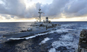 戰艦在日落時分航行於海洋，伴隨著戲劇性的雲層 — 郵輪 壁紙