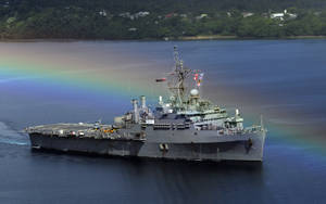 灰色軍艦在綠色海岸附近以彩虹為背景航行。