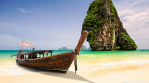 熱帶海灘上的木船，背景有綠色島嶼 — 海灘日落 壁紙