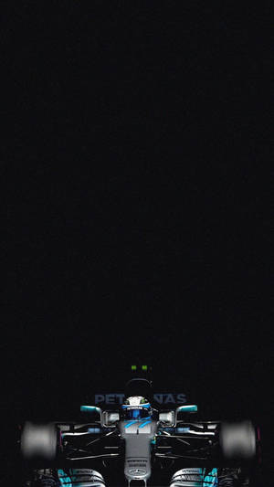 一輛一級方程式賽車在夜間被發光的綠色燈光照亮。 — F1 iPhone 壁紙