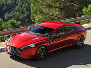 紅色Aston Martin跑車在山路上，有綠樹和護欄。 — 奧斯頓馬丁 壁紙