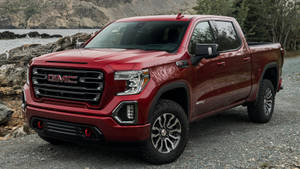 紅色GMC Sierra AT4皮卡車停在水和岩石附近。 — Gmc 壁紙