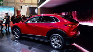 紅色Mazda CX-30 SUV在車展上於光亮地板上展示，有觀眾。 — 馬自達 壁紙