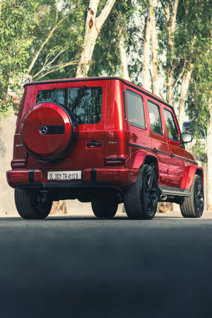 紅色賓士G-Class SUV停在綠樹成蔭的街道上。 — Mercedes Amg iPhone 壁紙