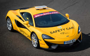 帶有British GT品牌標誌的黃色McLaren 570S安全車停在瀝青路面上。 — MacBook Pro 13 壁紙