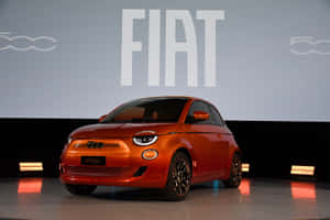 橘色Fiat 500e電動車在舞台上，後面有品牌標誌。 — 飛雅特 壁紙