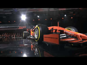 橘色一級方程式賽車在舞台上，配有明亮燈光和觀眾 — F1 2019 壁紙