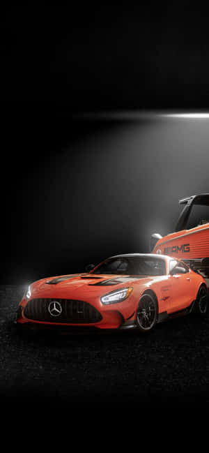 橙色 Mercedes-AMG GT 跑車在黑暗工作室中被聚光燈照亮。 — iPhone 16 壁紙