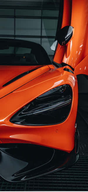 充滿活力的橙色McLaren跑車在現代車庫中打開車門。 — iPhone 18 壁紙