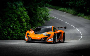 橙色McLaren賽車在彎曲的森林道路上行駛。 — 酷炫F1 壁紙
