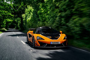 橙色McLaren在綠色森林道路上飛馳。 — 賽車 壁紙