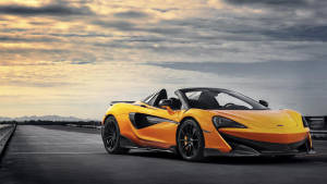 日落時分賽道上的橙色McLaren跑車與戲劇性的雲層。 — 麥拉倫 壁紙