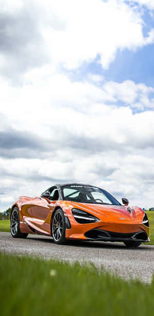 橙色McLaren 720S跑車停在碎石路上，周圍有綠草和多雲的天空。 — 4K 法拉利 壁紙
