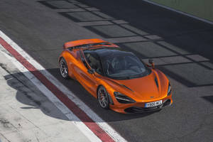 橙色McLaren 720S在明亮陽光下於賽道上疾馳。 — 4K 法拉利 壁紙
