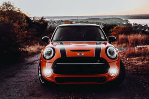 橙色MINI Cooper S停在日落時分的土路上，享有海岸景色和秋樹。 — 霓虹橘 壁紙