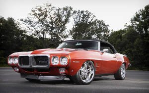 橙色Pontiac Firebird敞篷車停在戶外，背景有樹木。