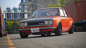 橙色和黑色經典Datsun跑車停在工業集裝箱附近。 — 高清汽車 壁紙