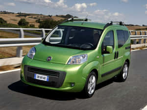 綠色Fiat Panda廂型車在晴朗藍天下行駛在風景如畫的鄉村道路上。 — 飛雅特 壁紙