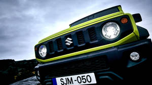多雲天空下，一輛萊姆綠色鈴木 Jimny SUV 在岩石地形上的特寫。 — 鈴木 壁紙