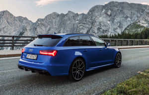 藍色 Audi RS6 Avant 在山路上行駛，背景有岩石山峰和樹木。 — Steam Deck OLED 壁紙